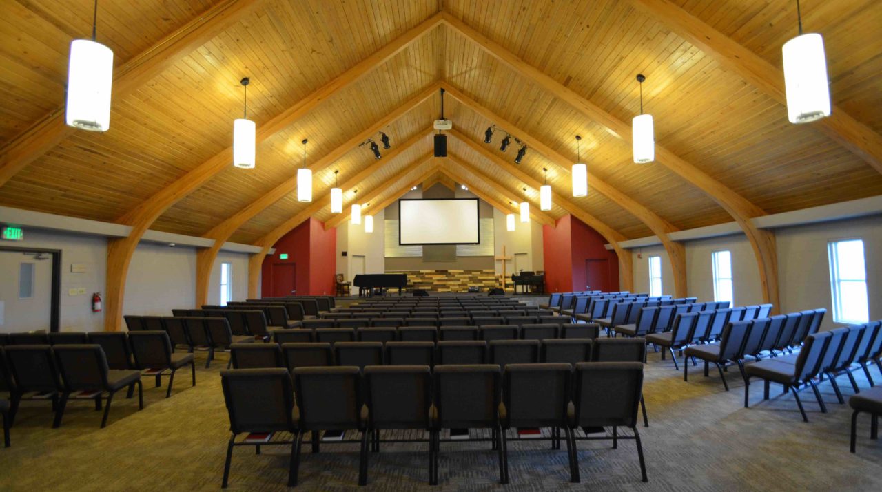 Calvary Community Baptist Church renovation Colorado. Mountain West Architects. Simple church design, simple church layout, minimalistic church layout, pendant lighting, exposed wood rafters in churches, wood ceiling in church. Spacious church stage. Large church screen. warm church color scheme