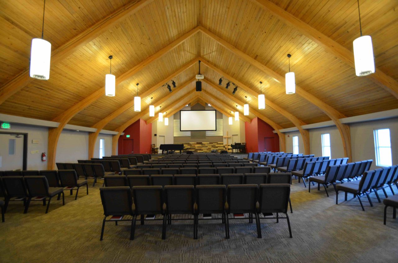 Calvary Community Baptist Church renovation Colorado. Mountain West Architects. Simple church design, simple church layout, minimalistic church layout, pendant lighting, exposed wood rafters in churches, wood ceiling in church. Spacious church stage. Large church screen. warm church color scheme