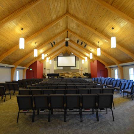 Calvary Community Baptist Church renovation Colorado. Mountain West Architects. Simple church design, simple church layout, minimalistic church layout, pendant lighting, exposed wood rafters in churches, wood ceiling in church. Spacious church stage. Large church screen. warm church color scheme
