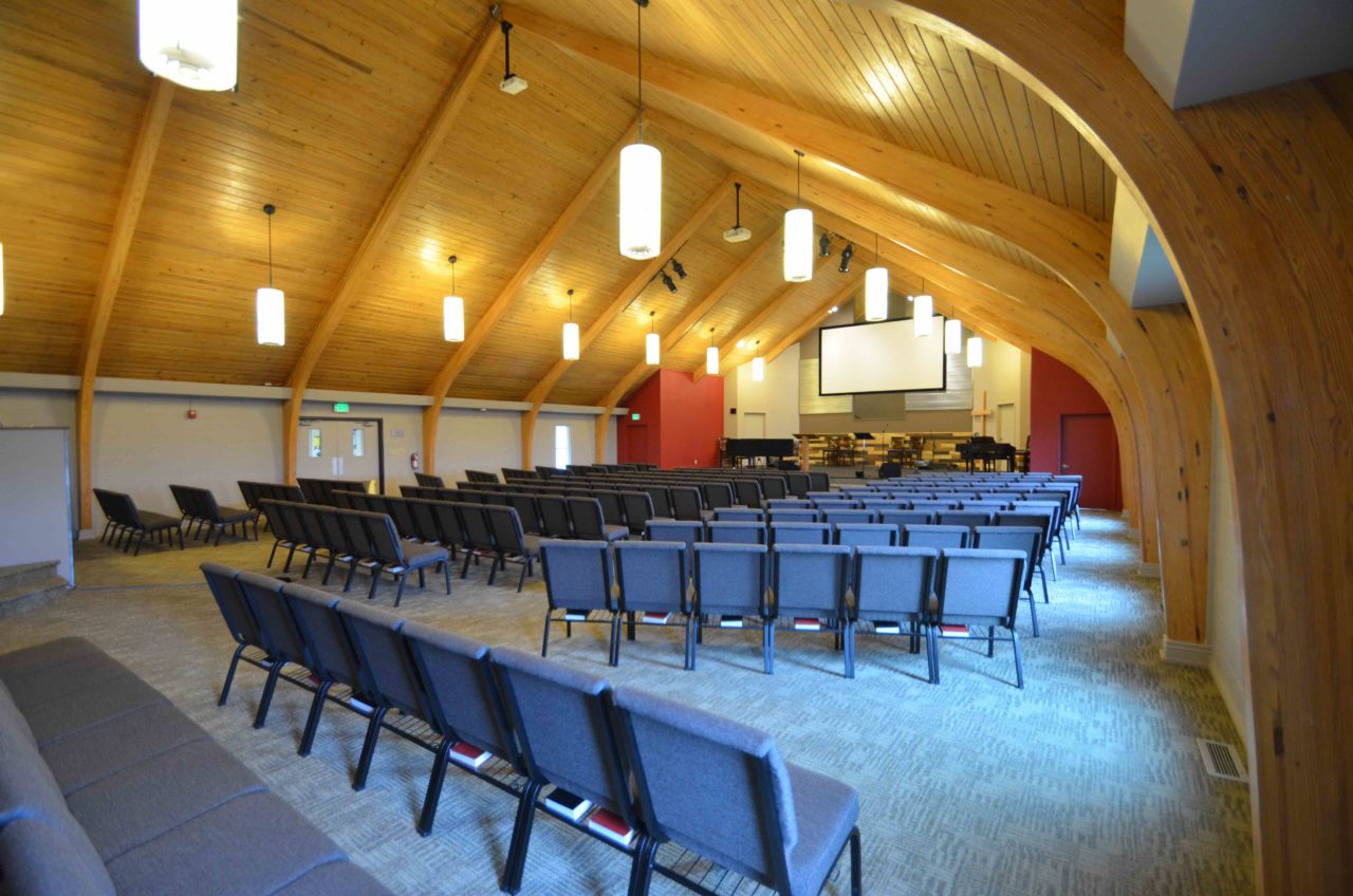 Calvary Community Baptist Church renovation Colorado. Mountain West Architects. Simple church design, simple church layout, minimalistic church layout, pendant lighting, exposed wood rafters in churches, wood ceiling in church. Spacious church stage. Large church screen. warm church color scheme