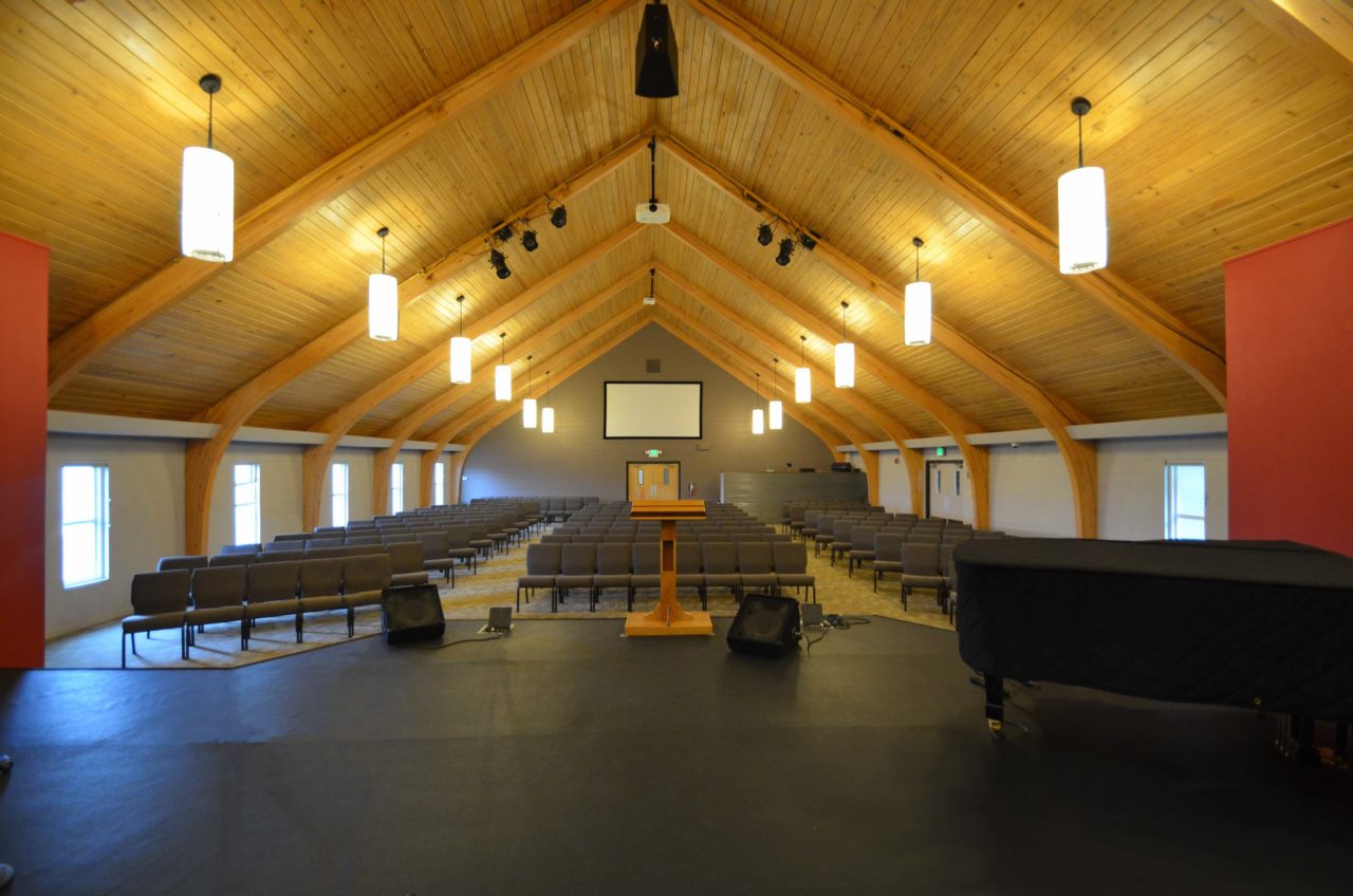 Calvary Community Baptist Church renovation Colorado. Mountain West Architects. Simple church design, simple church layout, minimalistic church layout, pendant lighting, exposed wood rafters in churches, wood ceiling in church. Spacious church stage. Large church screen. warm church color scheme