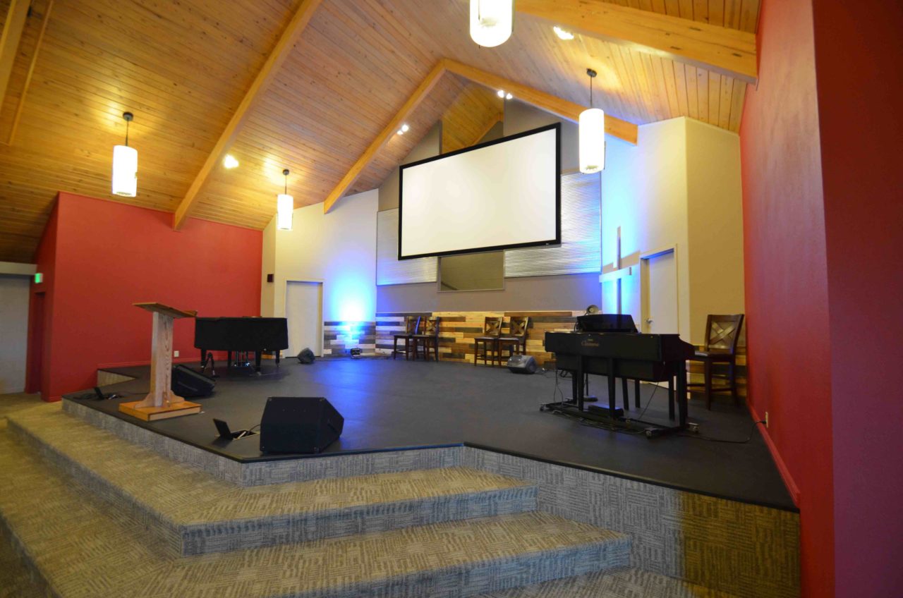 Calvary Community Baptist Church renovation Colorado. Mountain West Architects. Simple church design, simple church layout, minimalistic church layout, pendant lighting, exposed wood rafters in churches, wood ceiling in church. Spacious church stage. Large church screen. warm church color scheme