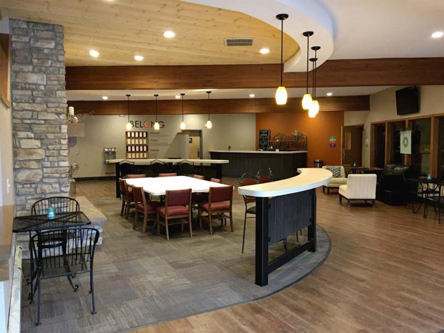 Pendant lightning, church foyer and lobby area, exposed wood framing, church café, warm church cafe color scheme, stone column, wood floor finish, wood ceiling